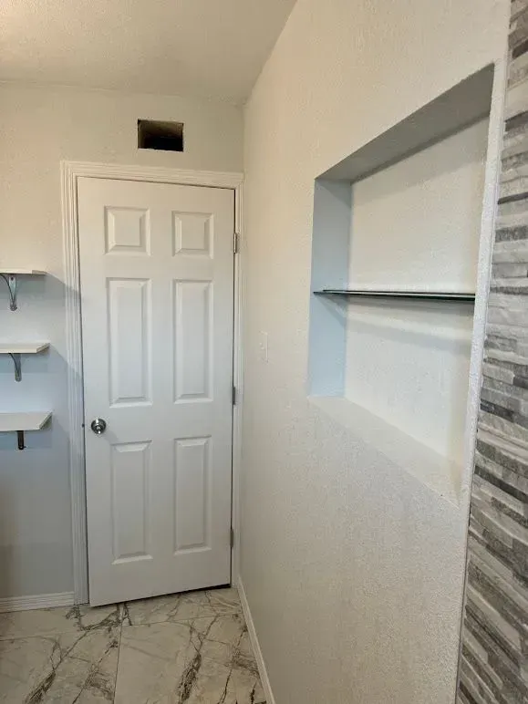 A bathroom with a door , shelves and a window.