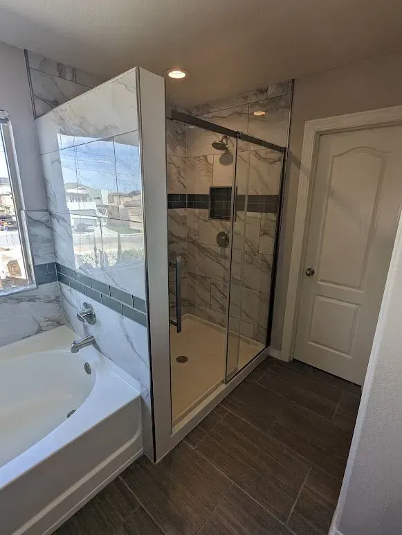 A bathroom with a tub and a shower with sliding glass doors.