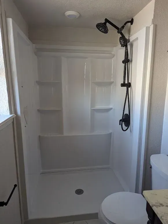 A bathroom with a shower , toilet and shelves.
