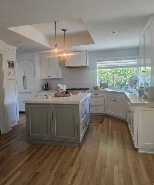 A kitchen with white cabinets and wooden floors and a large island in the middle.