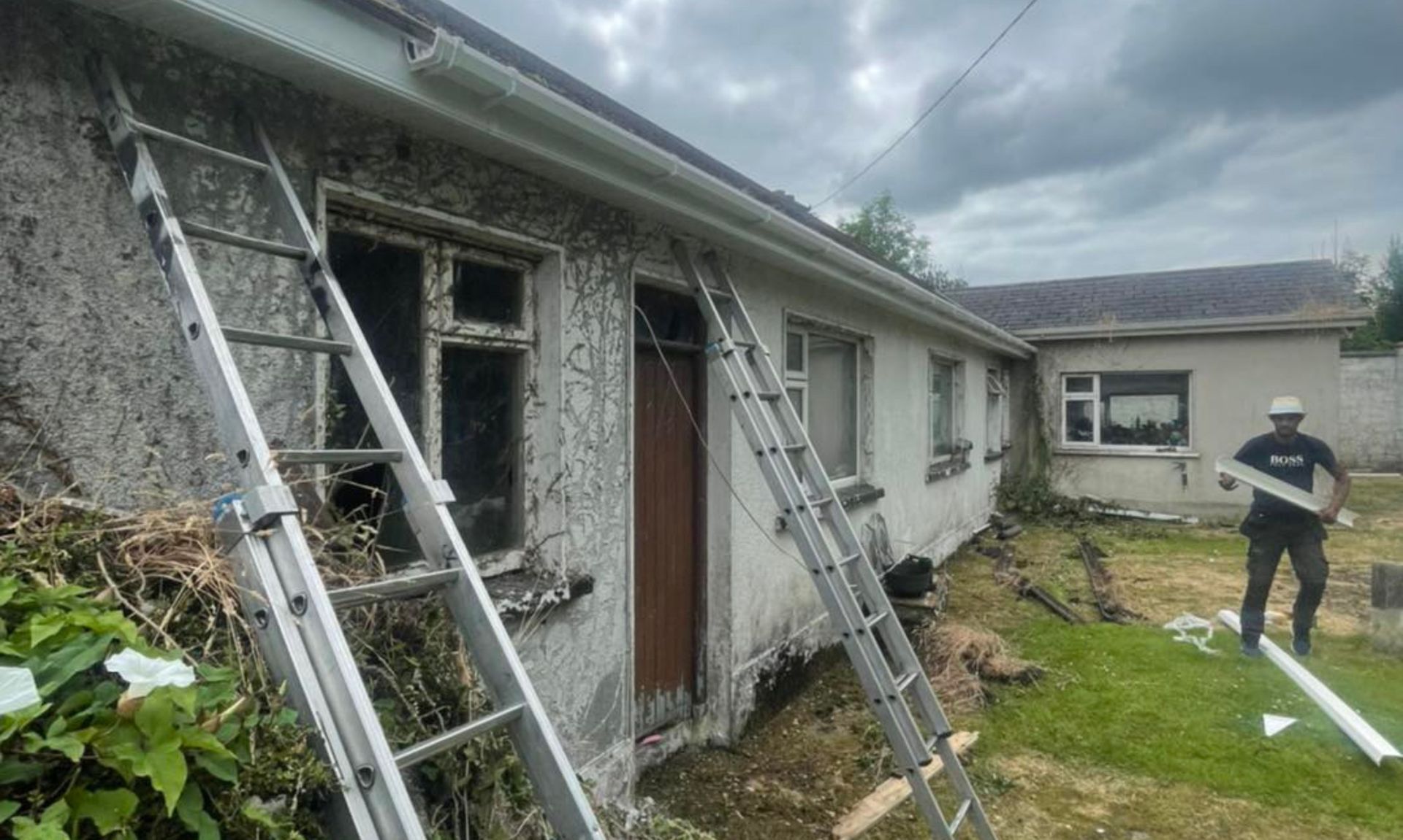 A man is standing in front of a house with a ladder.