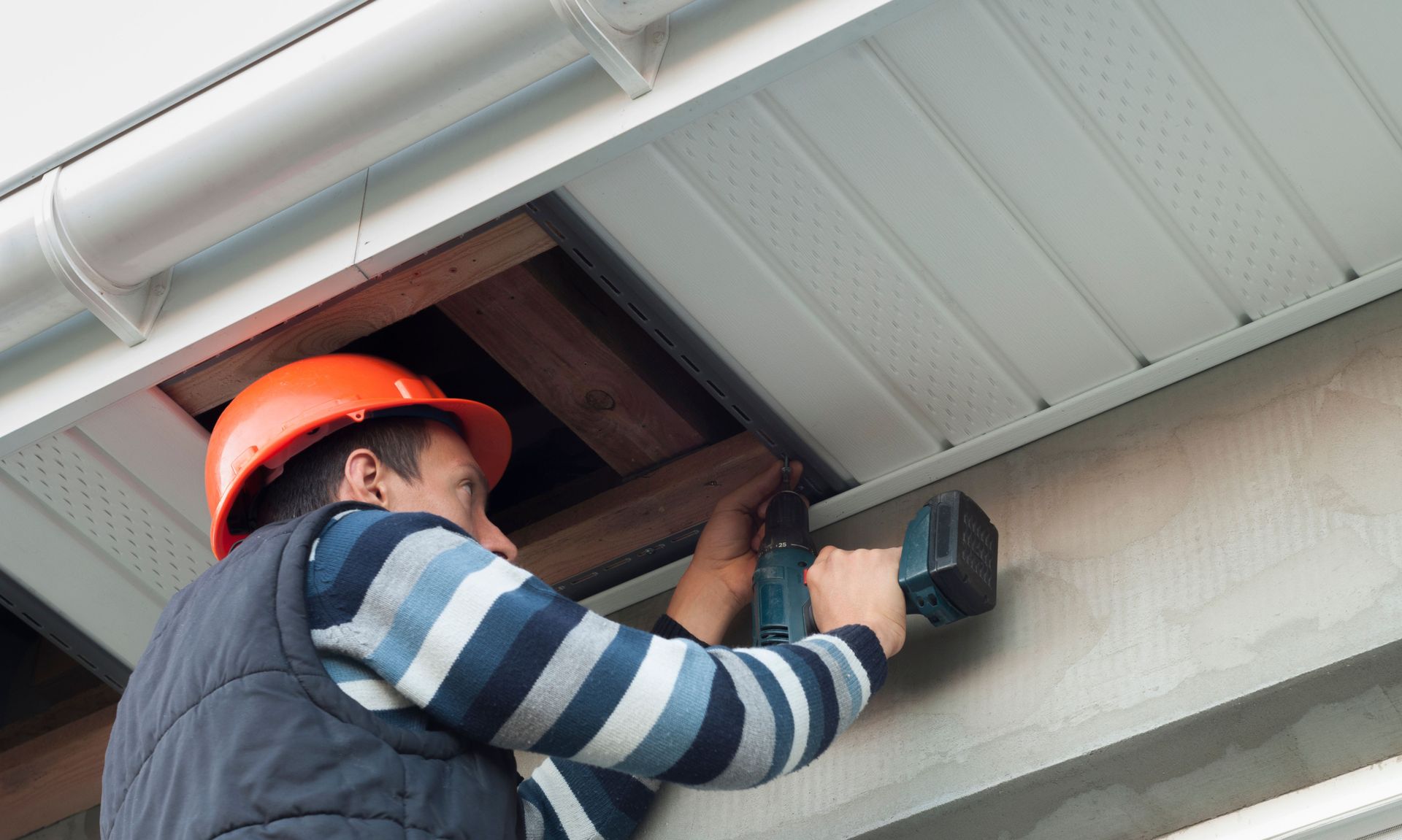 A man wearing a hard hat is working on the ceiling of a building.