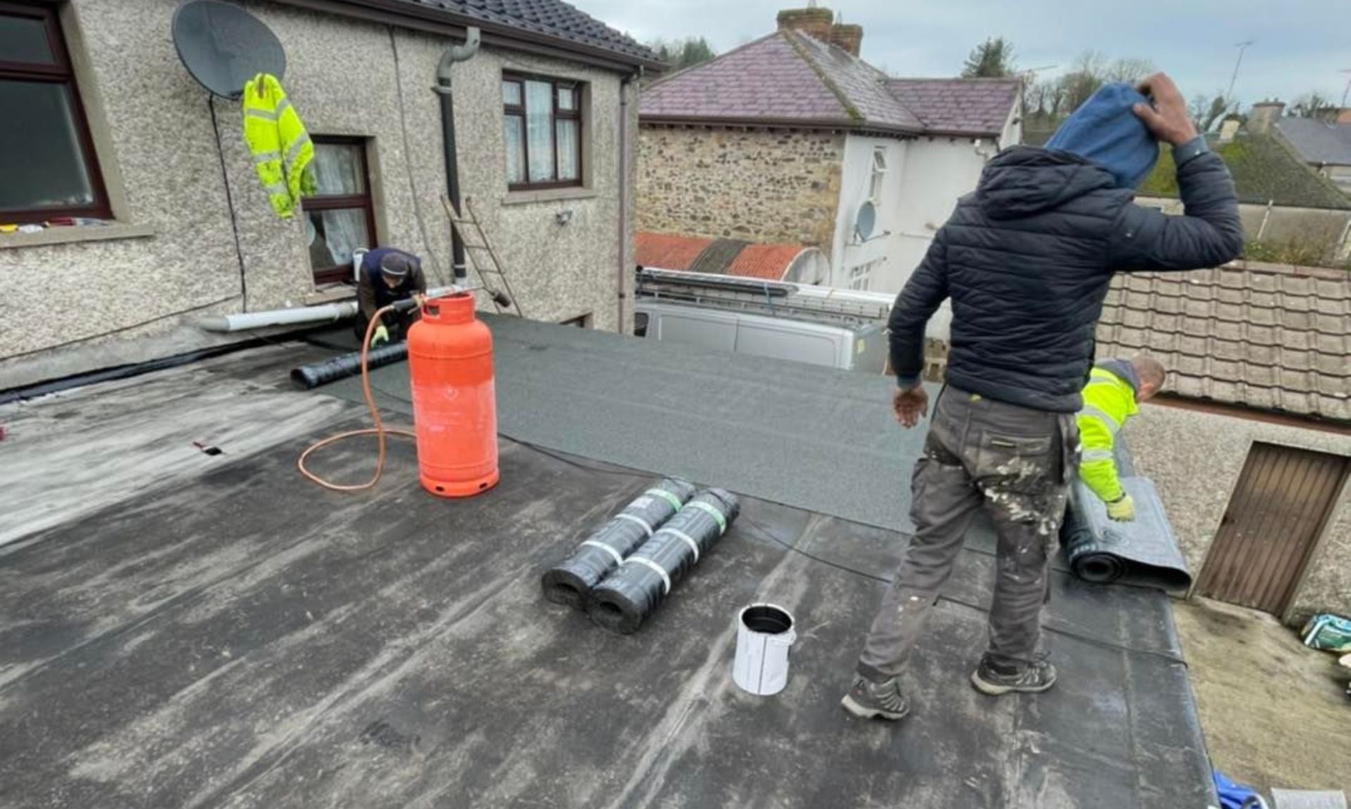 A man is standing on a roof next to a propane cylinder.