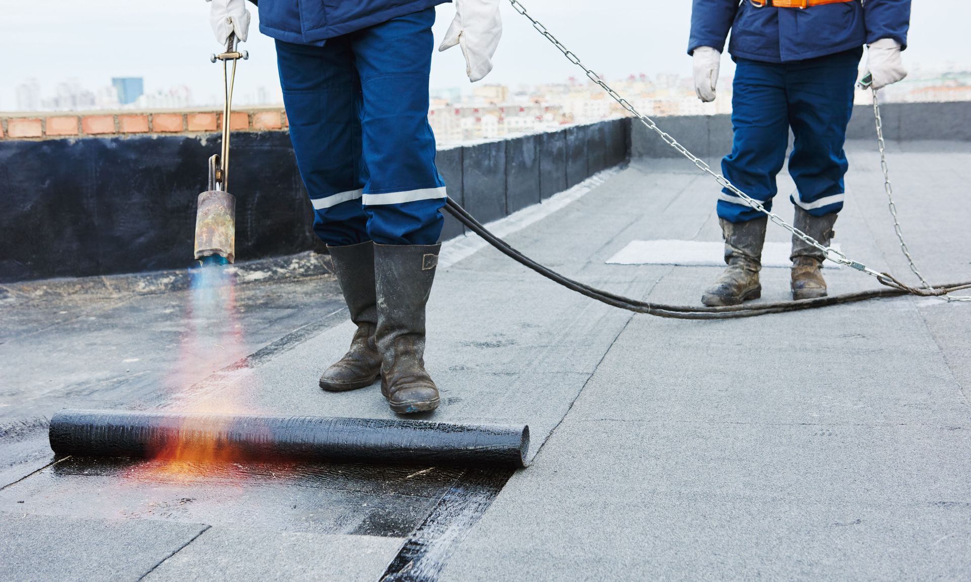 Two men are working on a roof with a torch.