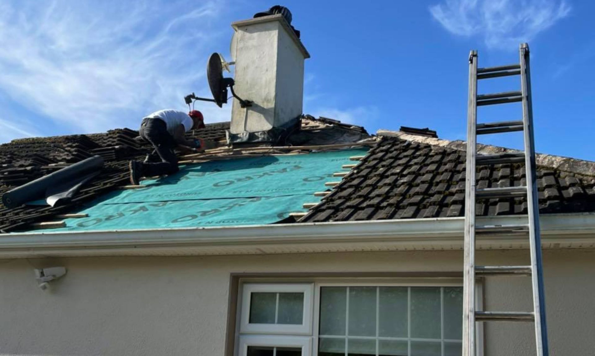 A man is working on the roof of a house with a ladder.
