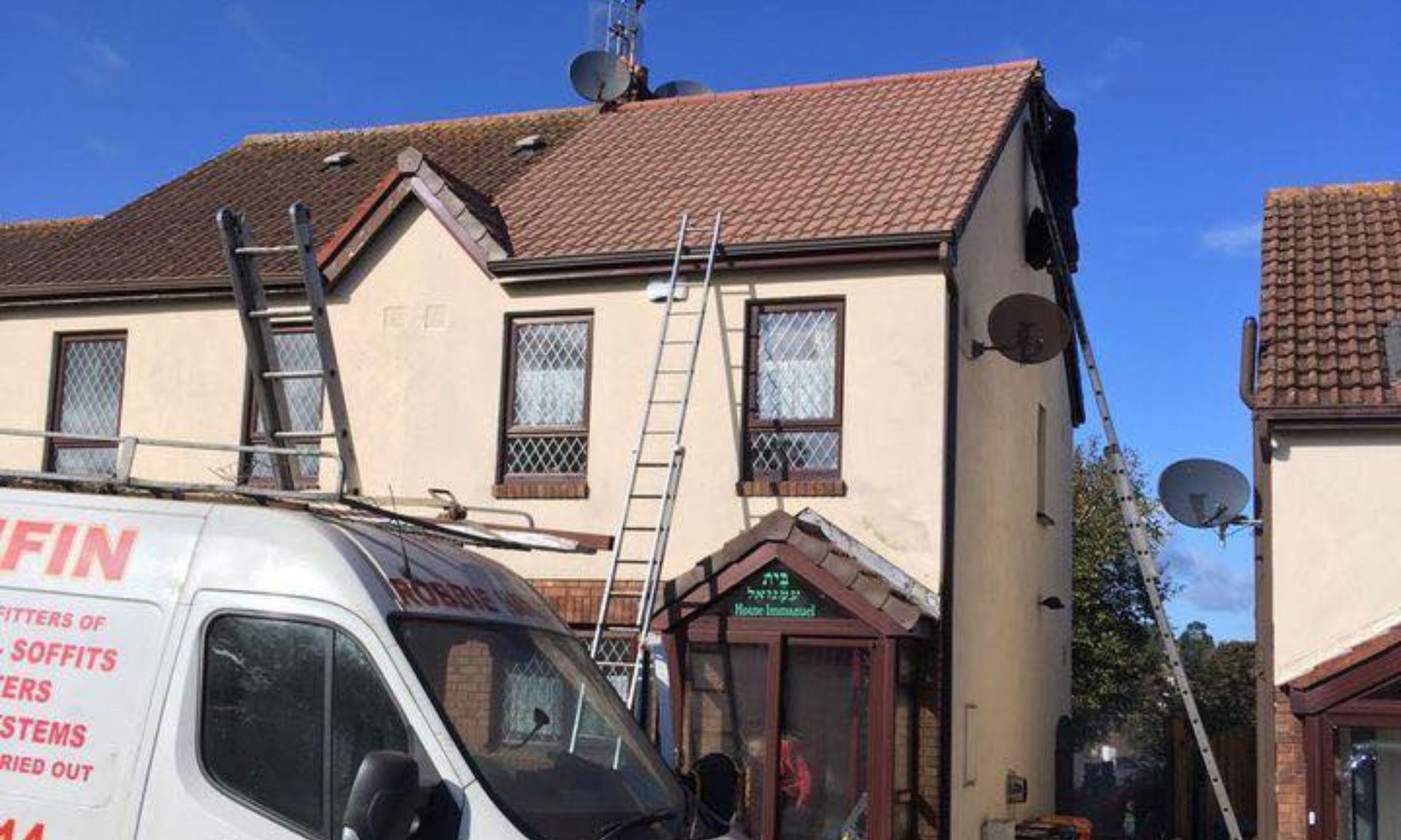 A white van with a ladder on top of it is parked in front of a house.