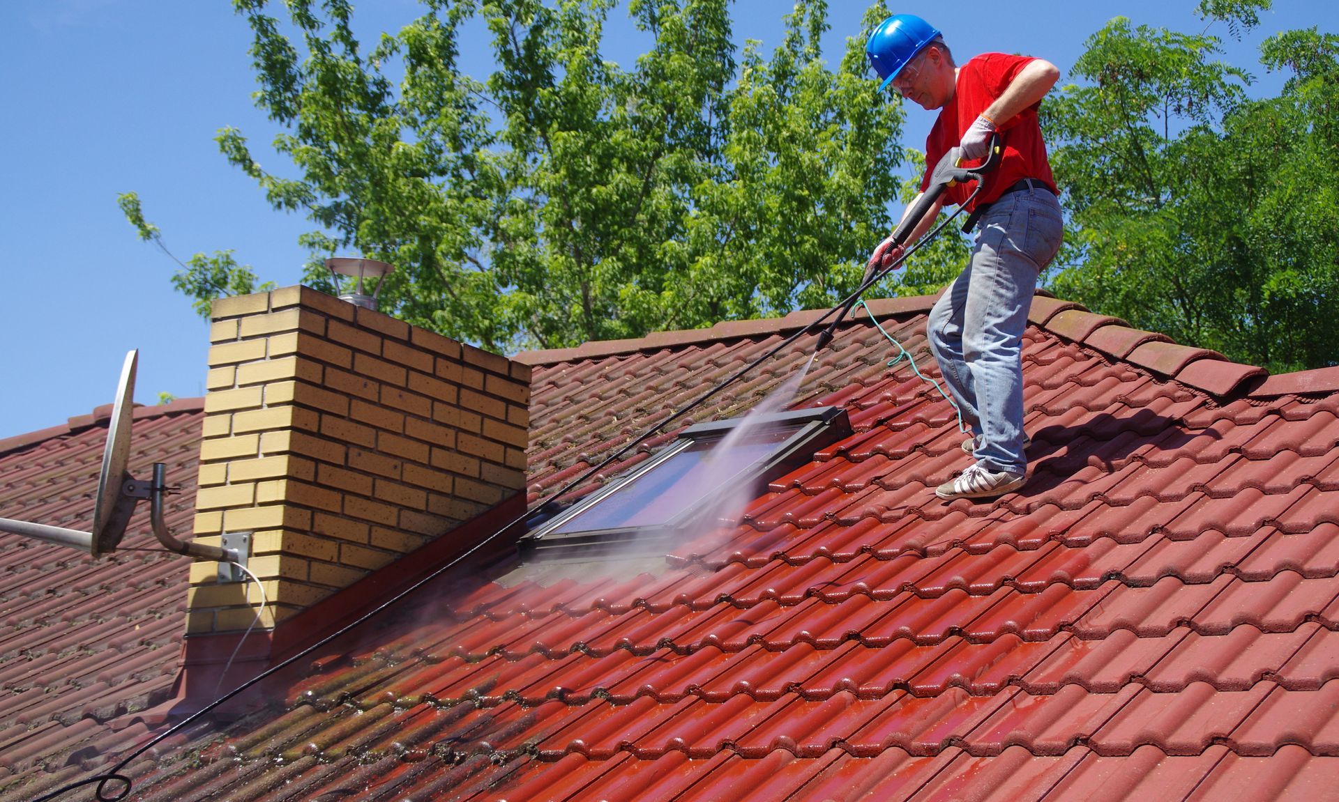 A man is cleaning the roof of a house with a high pressure washer