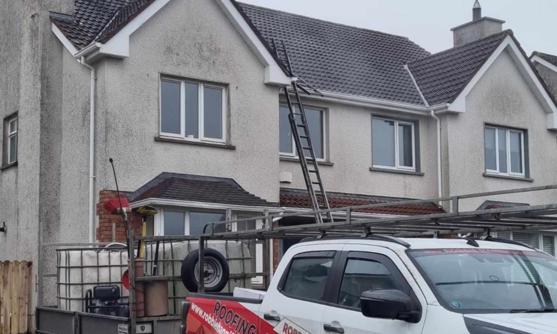 A white truck is parked in front of a house with a ladder on top of it.