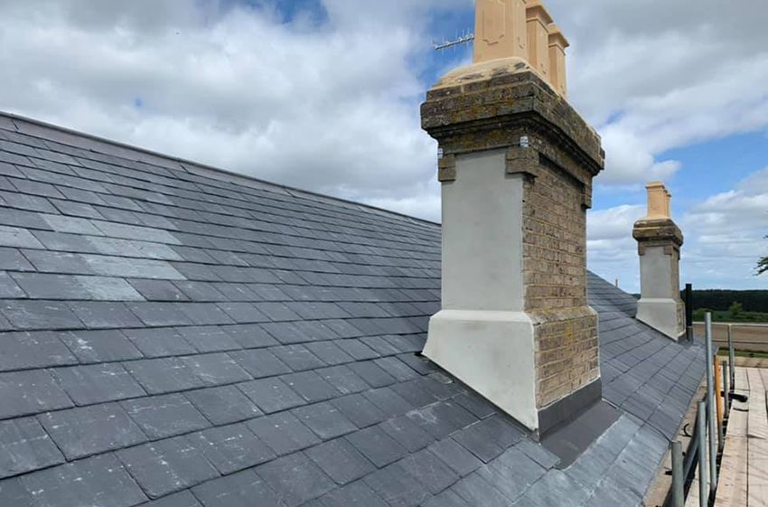 A man is kneeling on top of a roof fixing a chimney.