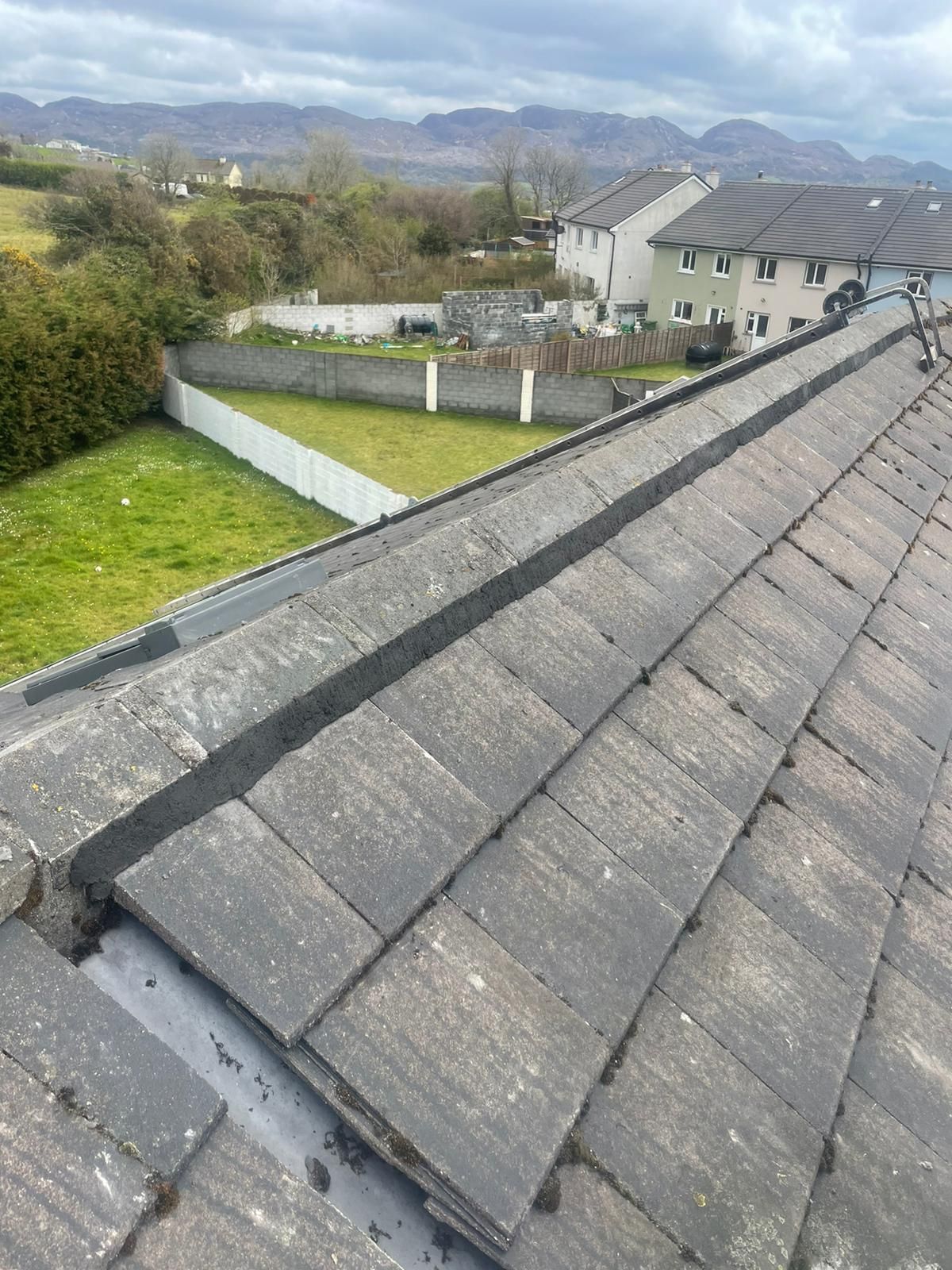 A man is kneeling on top of a tiled roof holding a hammer.