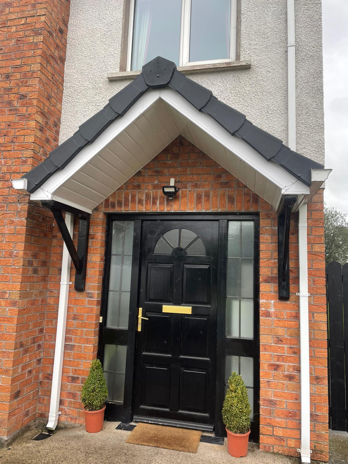 The front door of a brick house with a black door and a canopy over it.