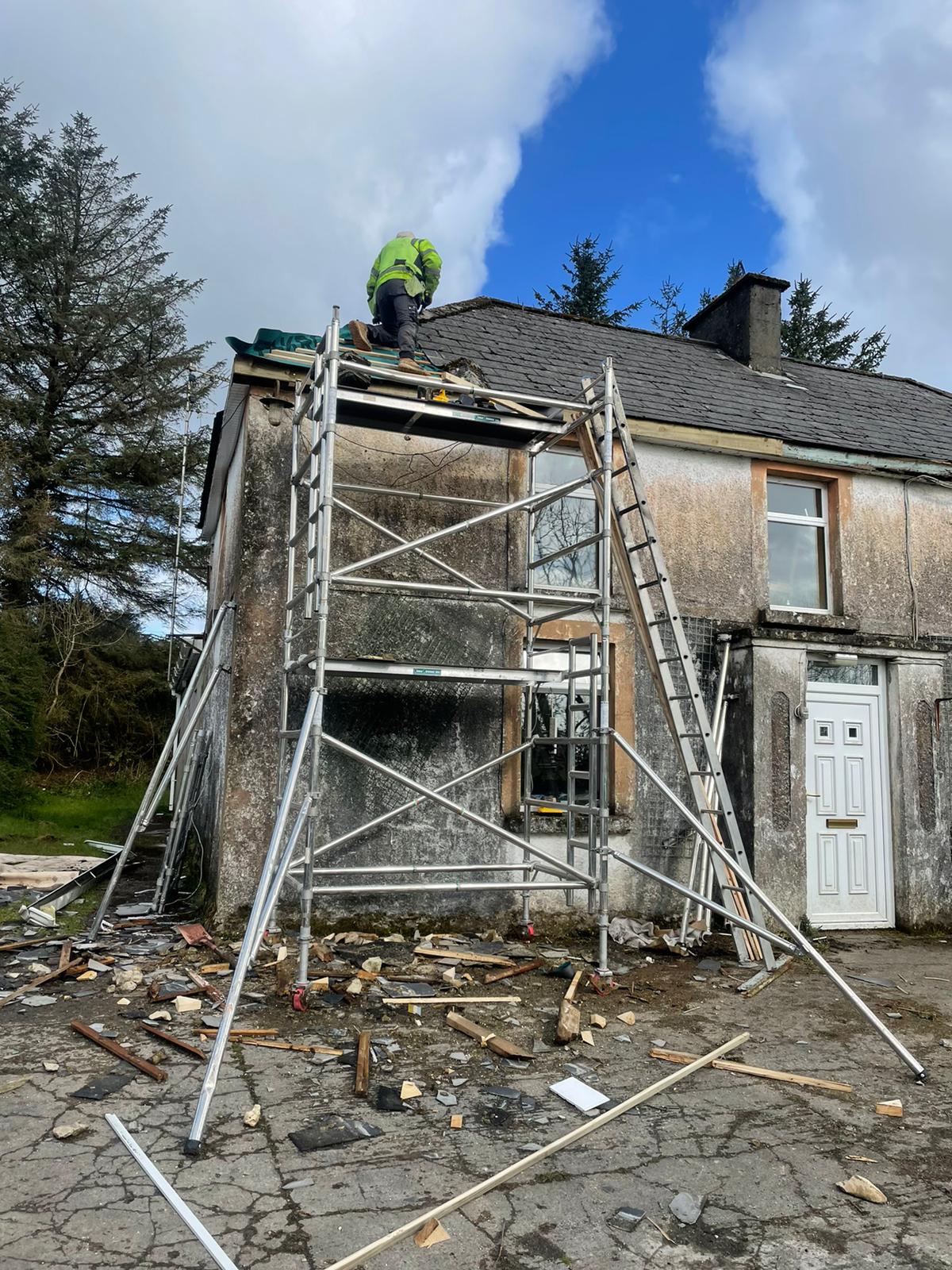 A man is working on the roof of a house on a scaffolding.
