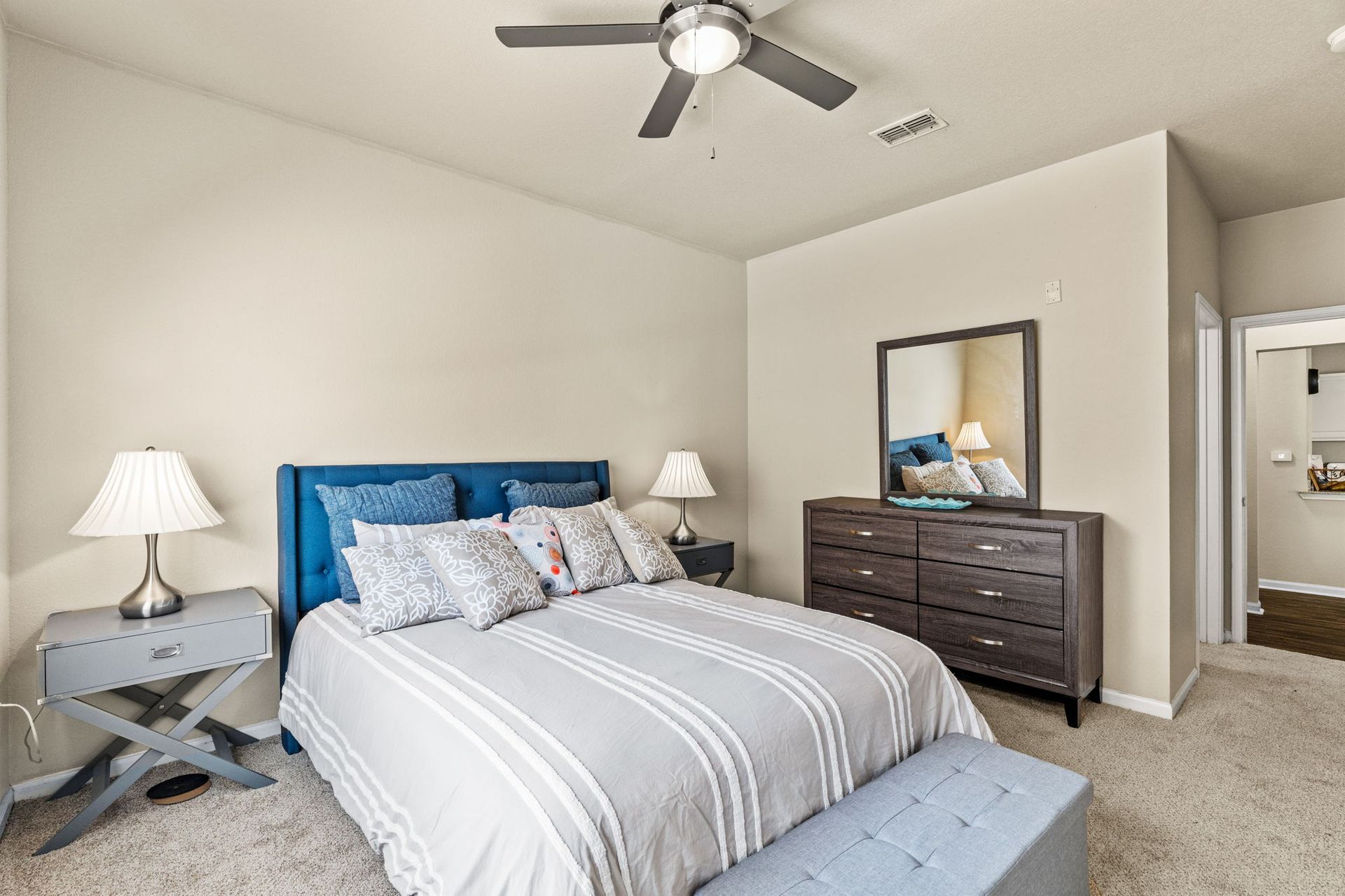 A bedroom with a bed , dresser , nightstand , mirror and ceiling fan at Reserve at Long Point.