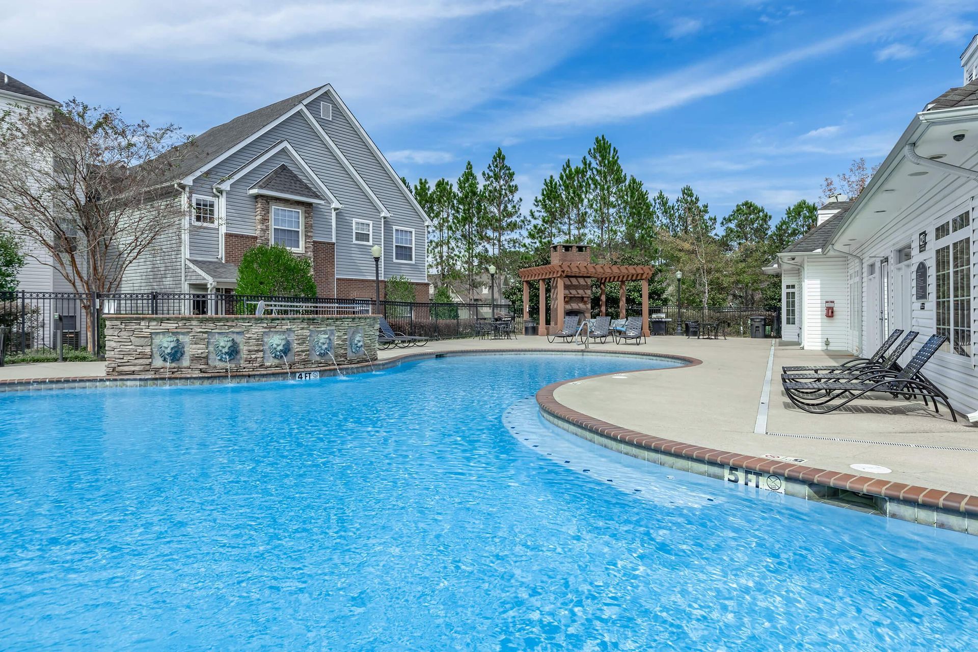 A swimming pool in a residential area on a sunny day, next to white and grey buildings.