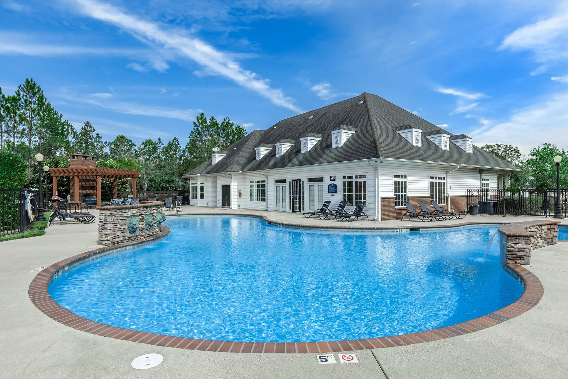 Pool with blue water, brick border, surrounded by concrete patio and apartment buildings.