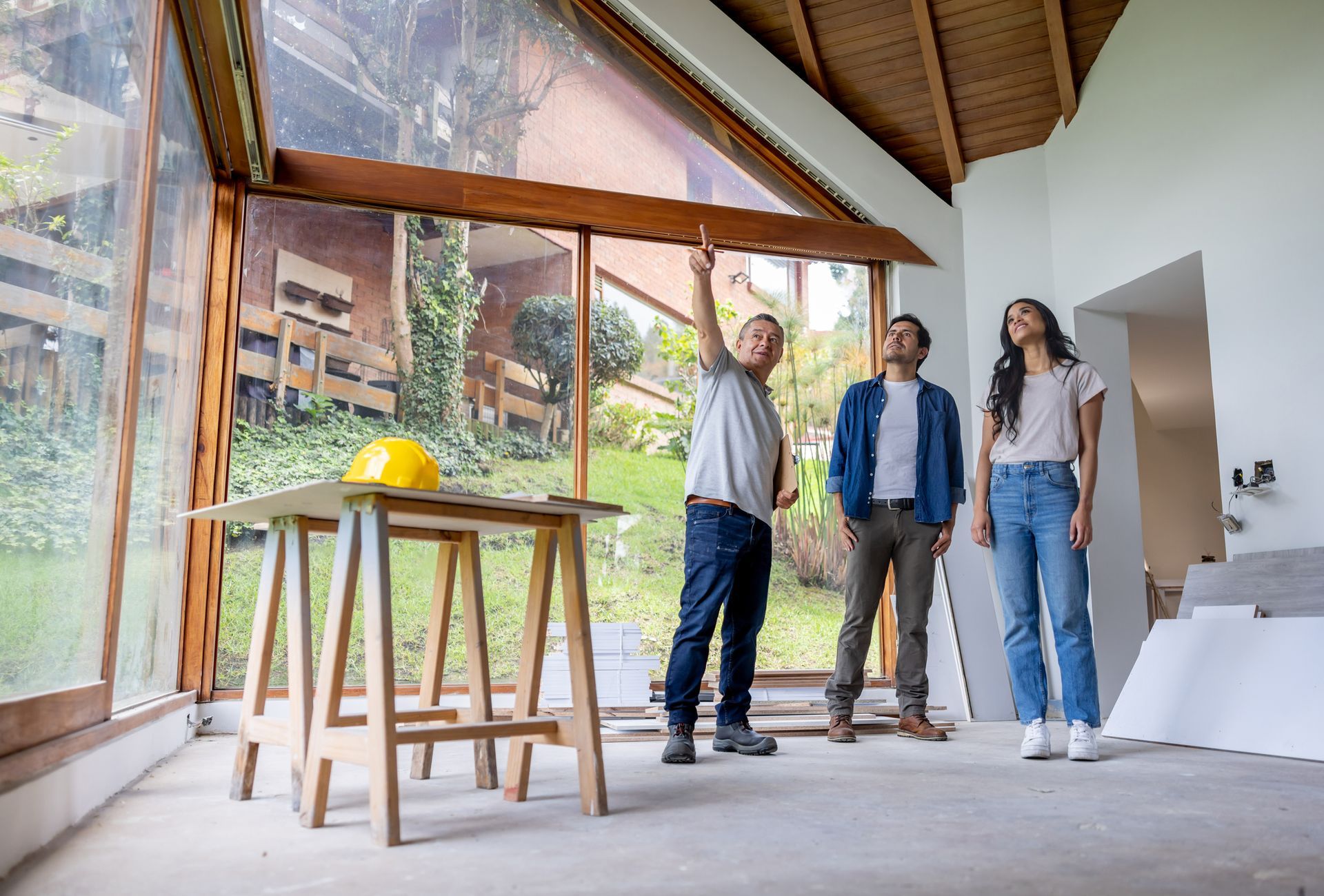 Three individuals stand inside an unfinished house, discussing home remodelling plans.