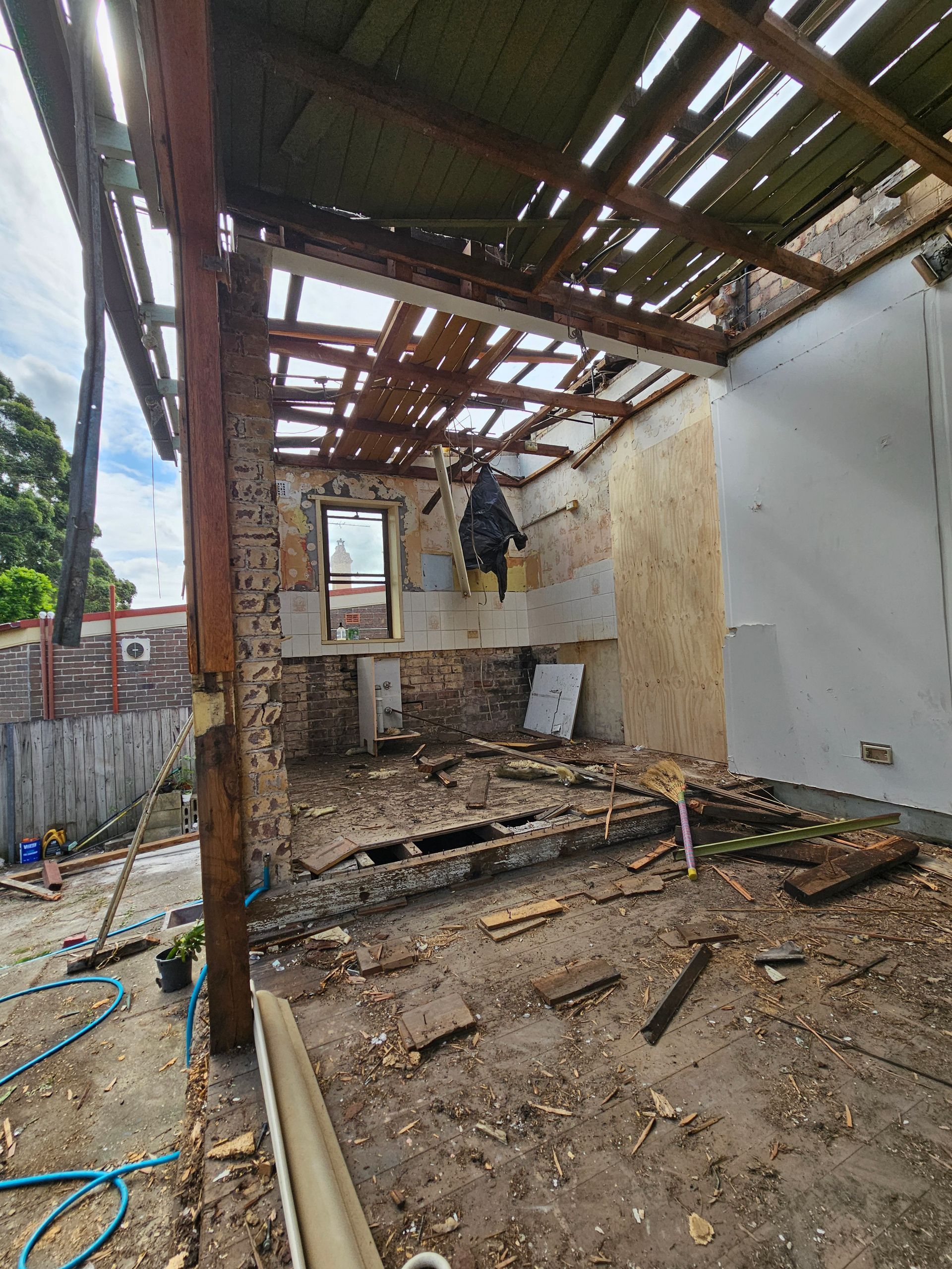 House demolition phase showing exposed beams, brick walls, and debris.