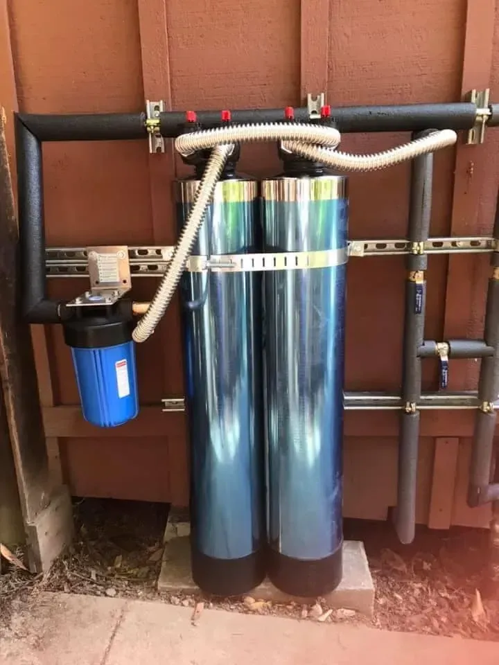 Outdoor water filtration system with blue filter tanks and black pipes mounted against a wall