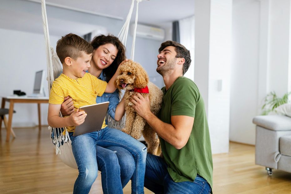 Family playing with a small dog in a bright living room, smiling and laughing together.