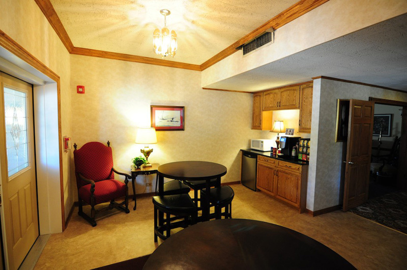 Interior hotel room with a seating area, kitchenette, and round tables.