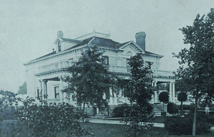 Large, two-story white house with columns, a porch, and a landscaped yard.