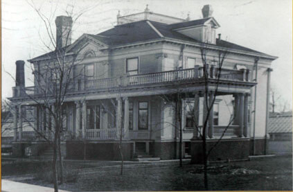 Two-story house with a porch and balcony. Trees in front, with two chimneys, in a black and white photograph.