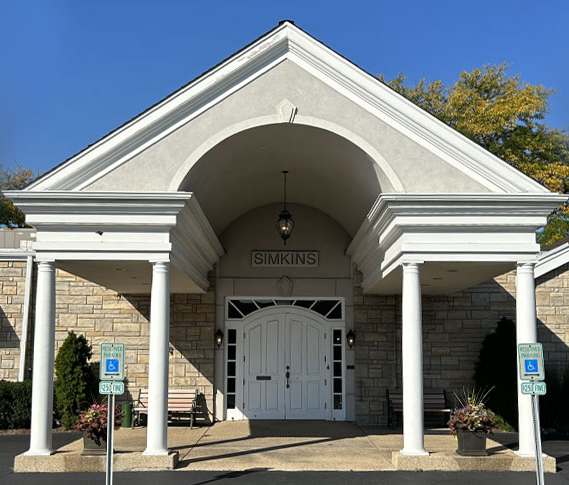 Exterior of a building with white columns and arched entrance. Stone facade. Accessible parking signs present.