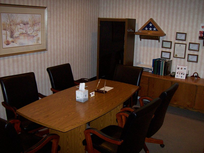Office meeting room with a wooden table, black chairs, and a cabinet holding a folded American flag.