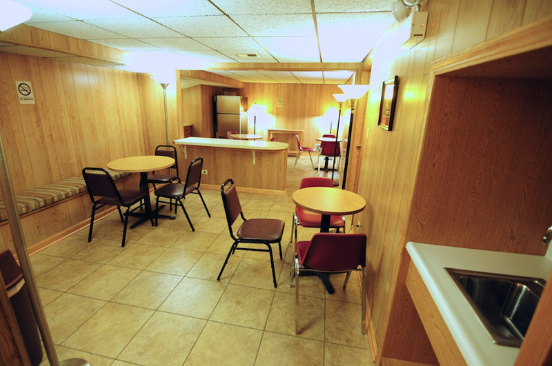 Basement lounge with tables, chairs, bar, refrigerator, and sink; wood paneling.