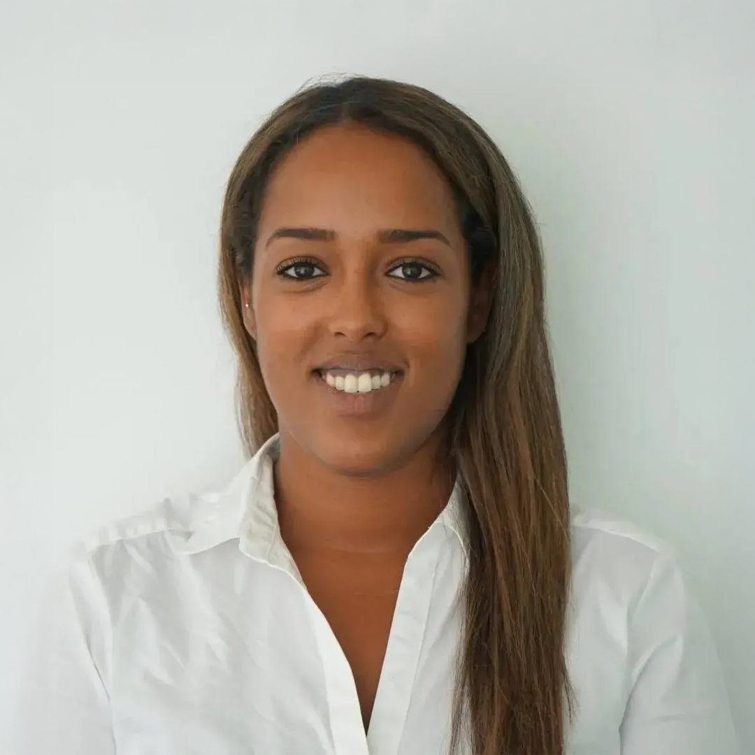 Woman in white shirt smiling at the camera. Neutral background.