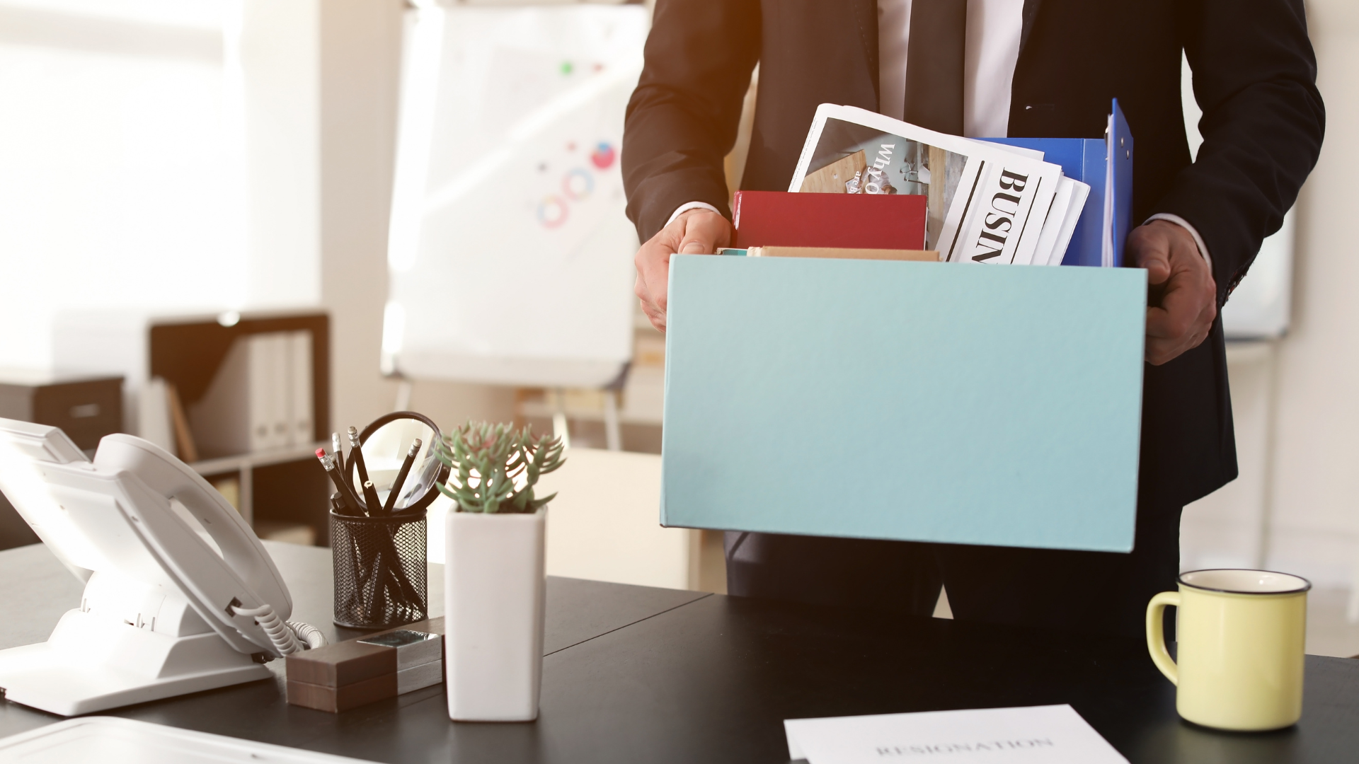 Person in a suit holding a box of office belongings, likely leaving work.