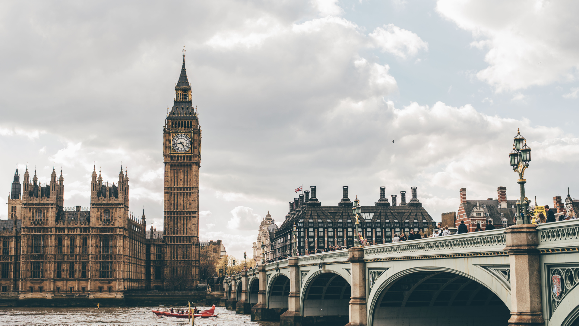 Big Ben and the Houses of Parliament in London, seen from a bridge, cloudy sky above.