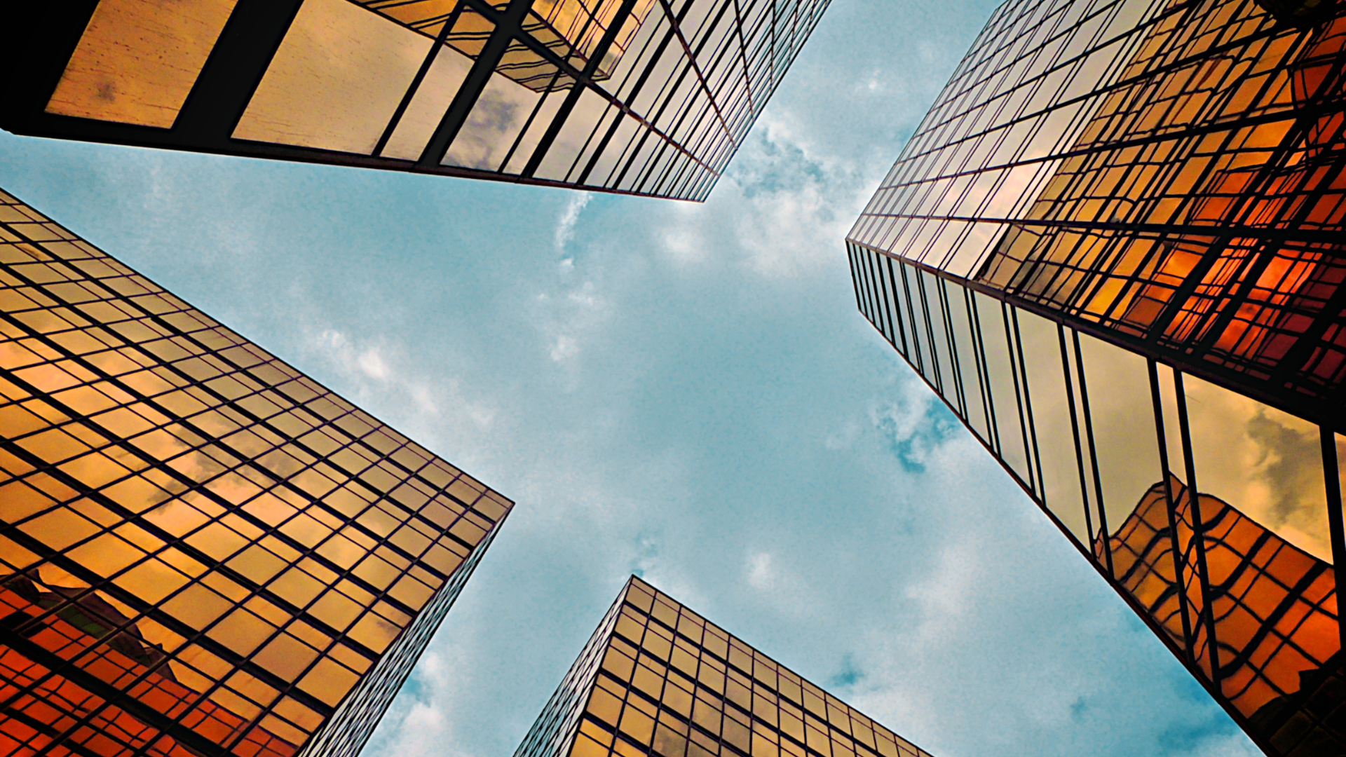 Golden skyscrapers reaching towards a blue sky, viewed from below.
