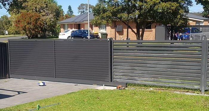 Dark gray sliding driveway gate and matching fence in front of a suburban house on a sunny day  — FBM Fabrication In Dapto, NSW