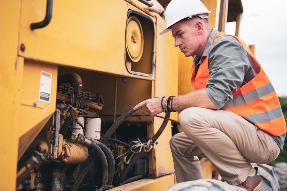 A Man Is Kneeling Down to Look at The Engine of A Construction Vehicle — FBM Fabrication In Dapto, NSW