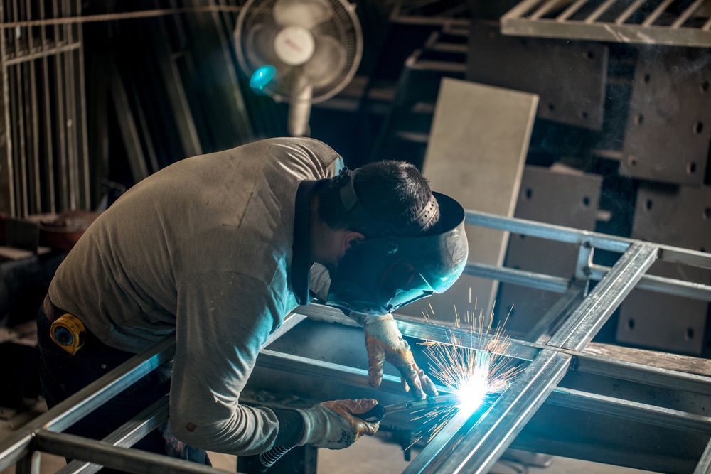 A Man Is Welding a Metal Frame in A Factory — FBM Fabrication In Dapto, NSW