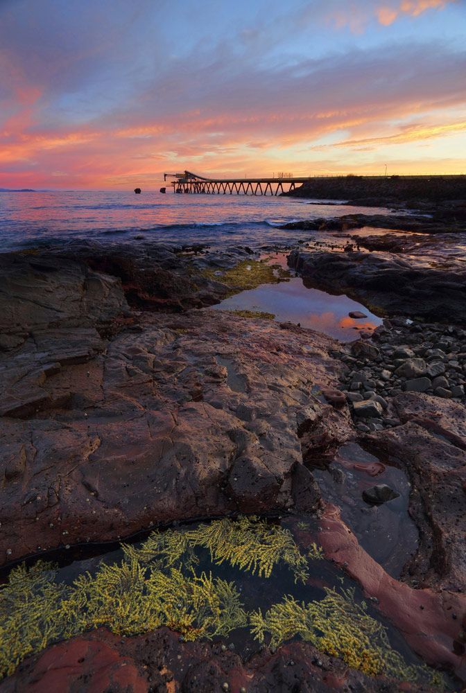 A Sunset Over a Rocky Beach with A Boat in The Distance — FBM Fabrication In Shellharbour, NSW