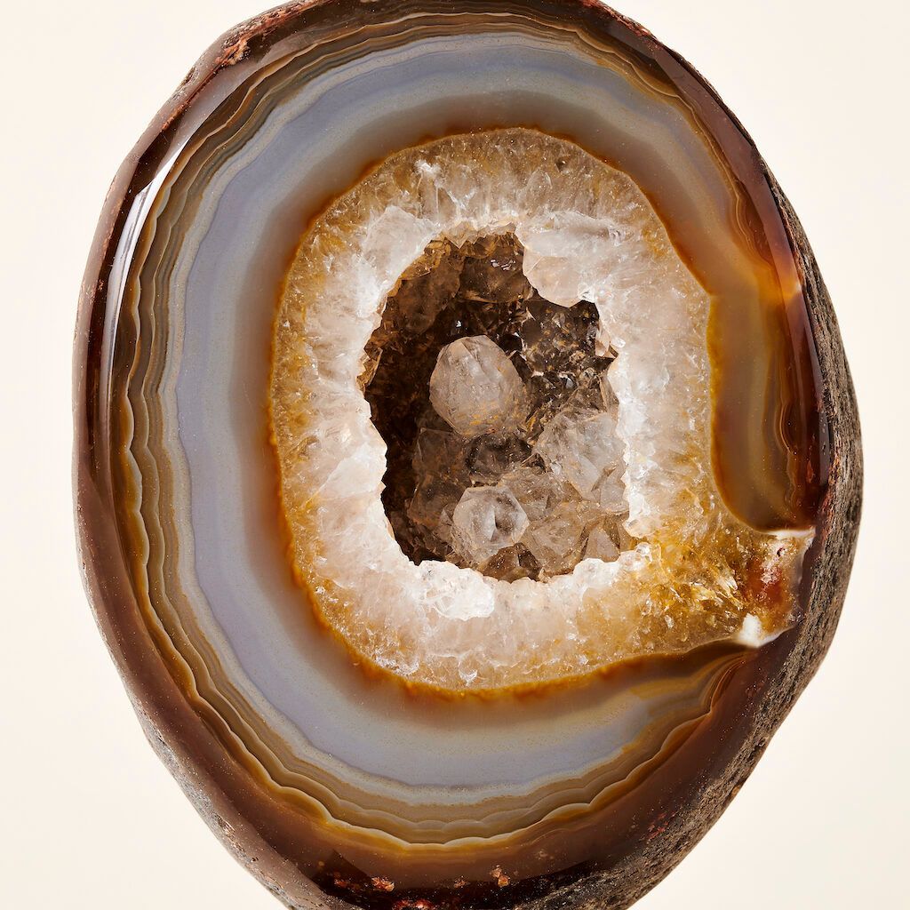 Een dwarsdoorsnede van een geode met bruine en grijze agaatbanden rond een centrum van sprankelende, doorschijnende kristallen.