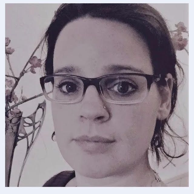 Een persoon met een bril kijkt in de camera tegen een witte achtergrond met wazige decoratieve bladeren.