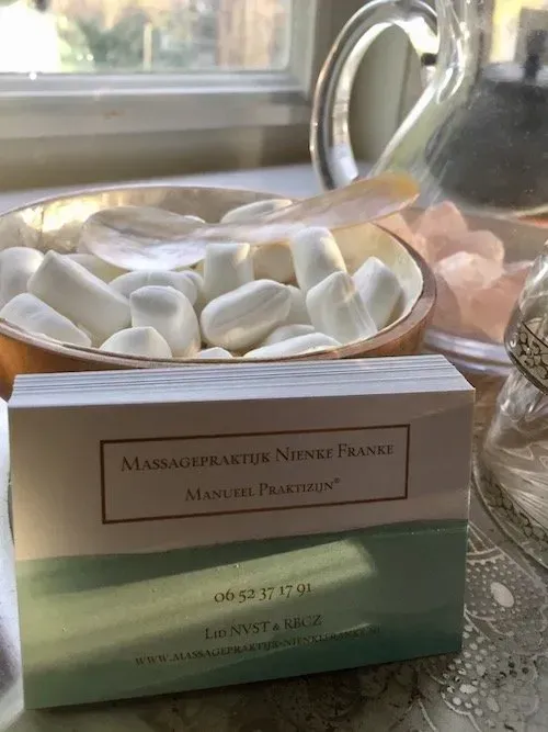 Een visitekaartje van Nienke Franke, een massagetherapeute, ligt voor een schaal met witte marshmallows.