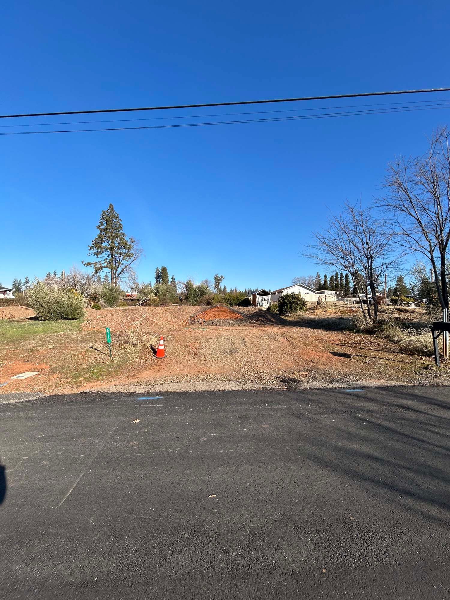 Vacant dirt lot under a bright blue sky, with a distant house visible; trees line the horizon.