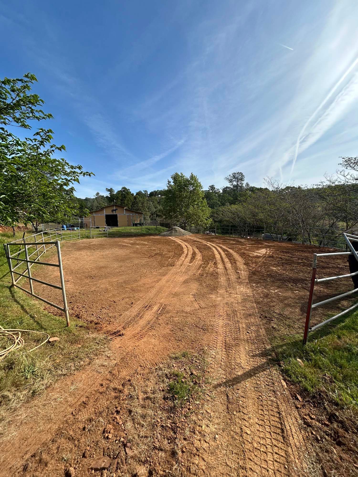 Dirt driveway leading to a barn under a blue sky; two open metal gates.