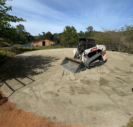 Bobcat skid-steer on a gravel surface, with a barn in the background under a blue sky.