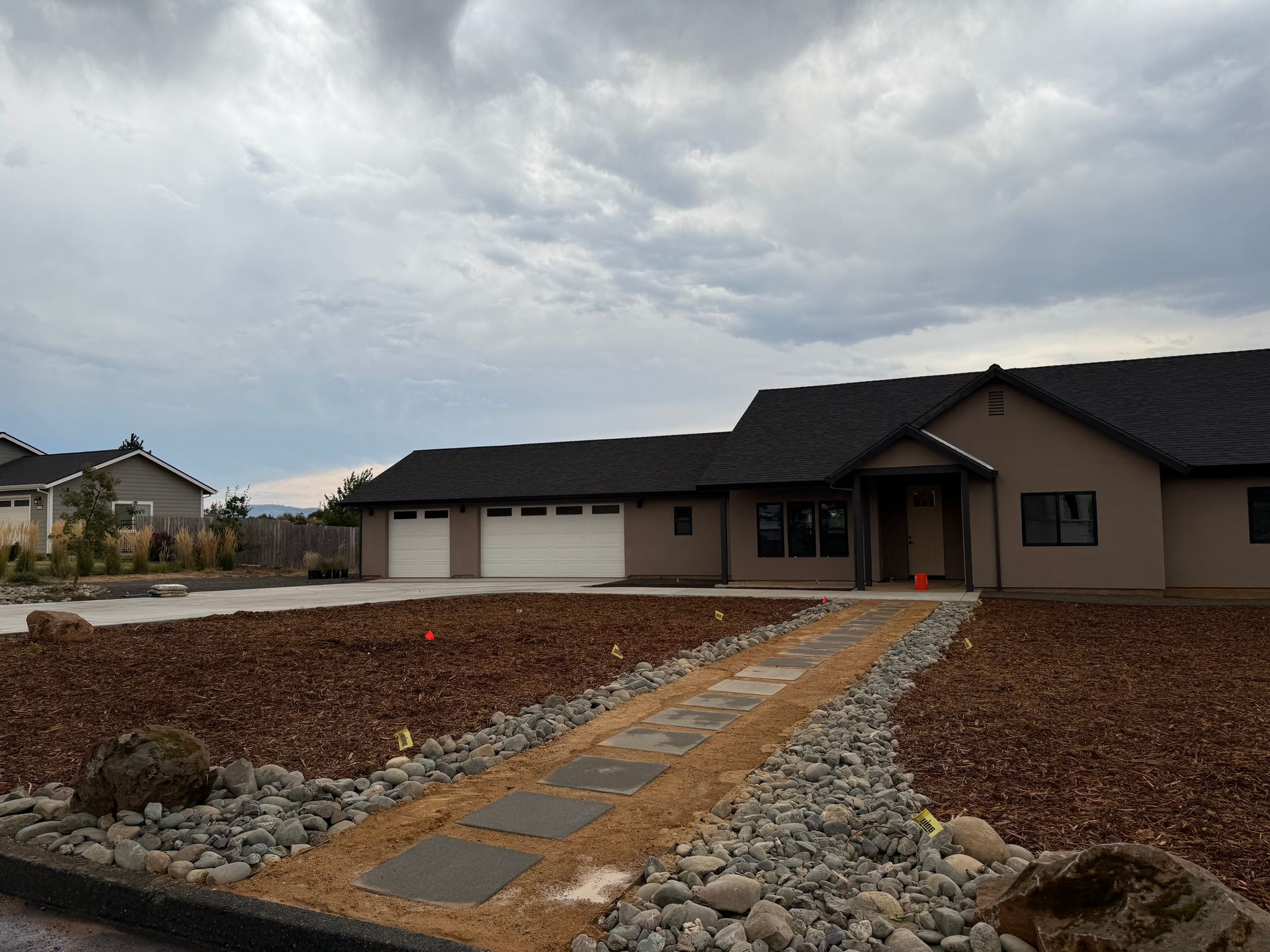 Tan ranch house with attached garage and stone walkway on a cloudy day.