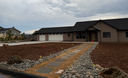 Tan house with a black roof and a stone path leading to the entrance. Overcast sky.