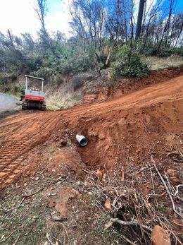A small excavator on a hillside, red soil, and a drainage pipe visible.