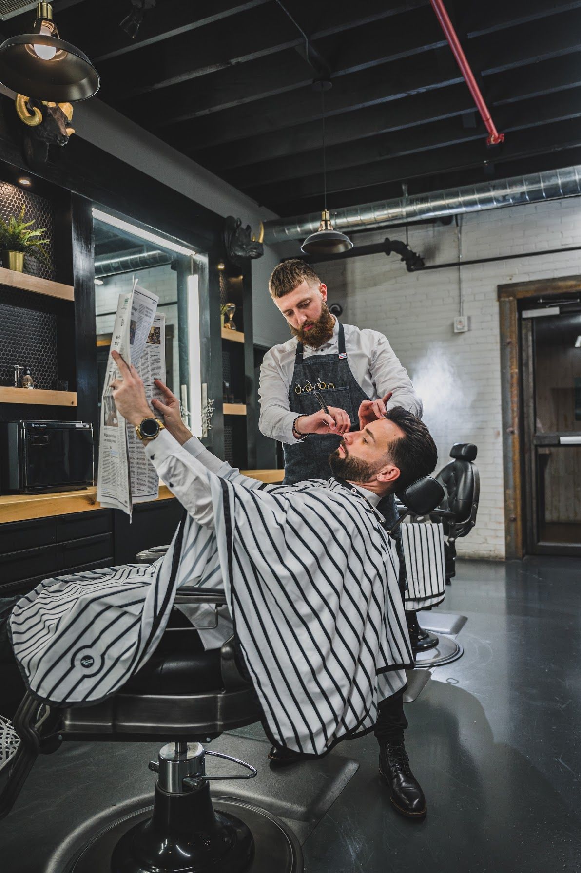 A barber cutting a man's short hair in a salon; the barber is wearing a hat and patterned shirt.