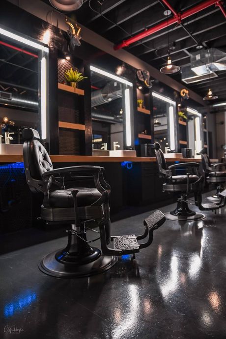 Barbershop interior with black chairs, mirrors, and dark surfaces.