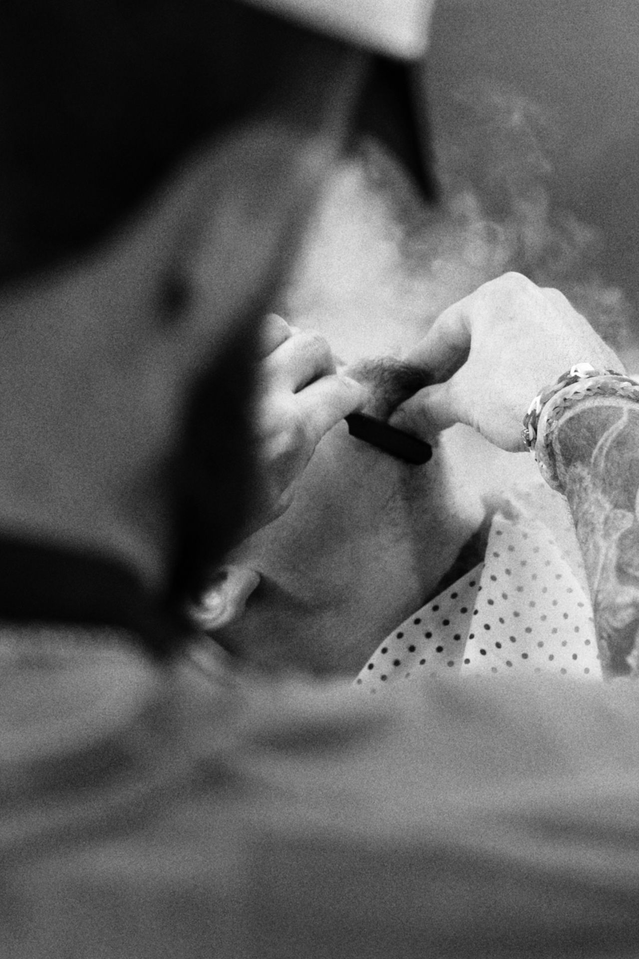 Person lighting a cigarette for another, close-up, black and white.