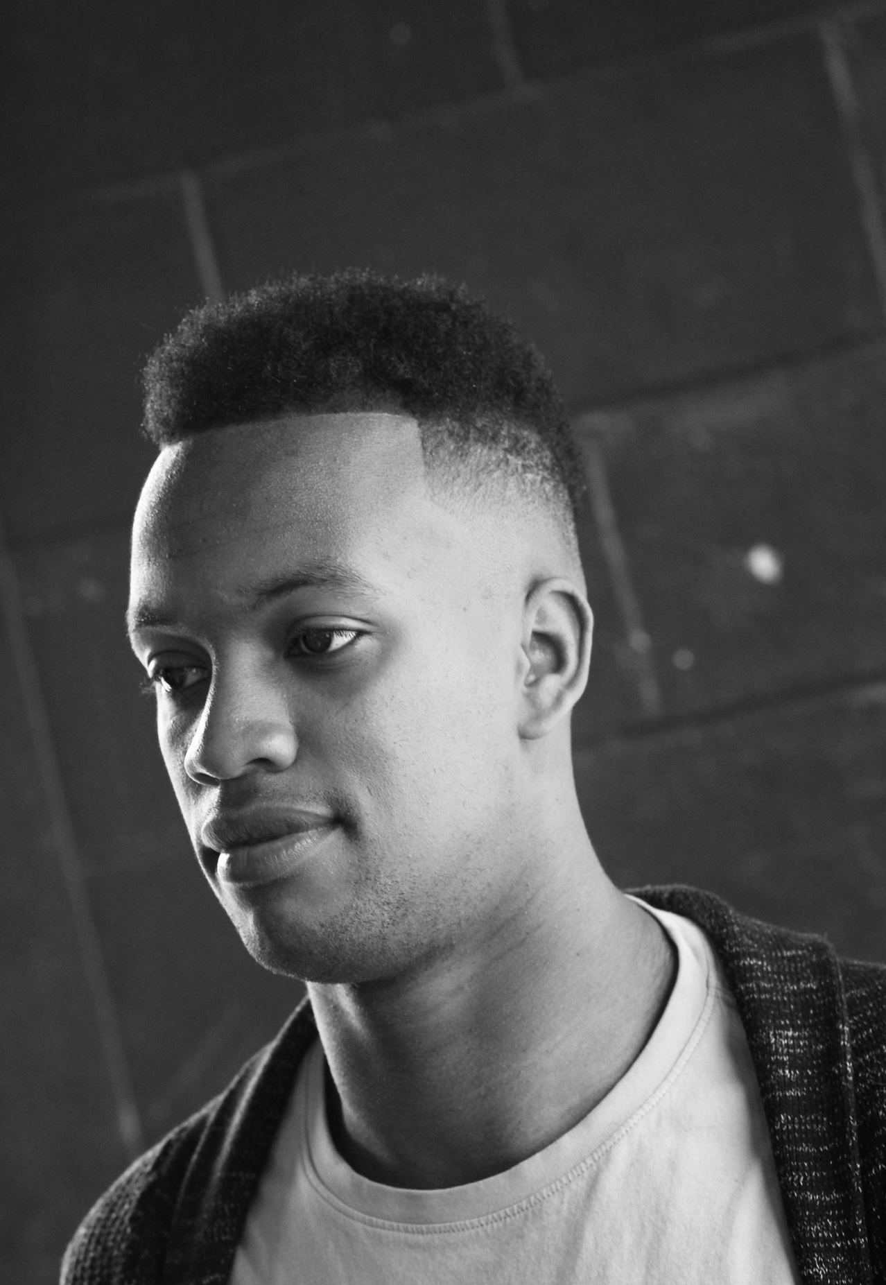 Young Black man with fade haircut, looking to the side, wearing a cardigan.